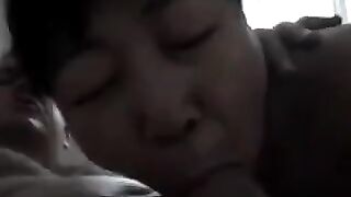 An old Chinese woman practices her blowjob skills on a young guy’s bed
